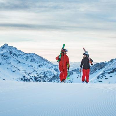 Zwei Skifahrer gehen mit Skiern über eine präparierte Piste in den Alpen